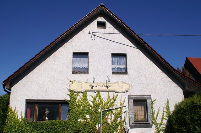 Weißes Haus mit Satteldach und dem Schild Die Landsauna über dem Fenster.