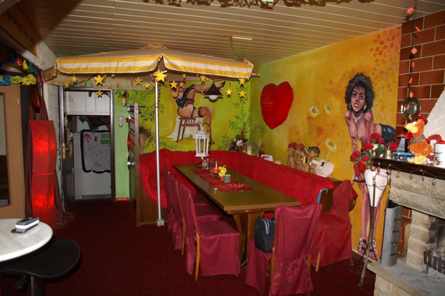 Sitzbereich mit langem Tisch, roten Stühlen und einer gelben Wand.