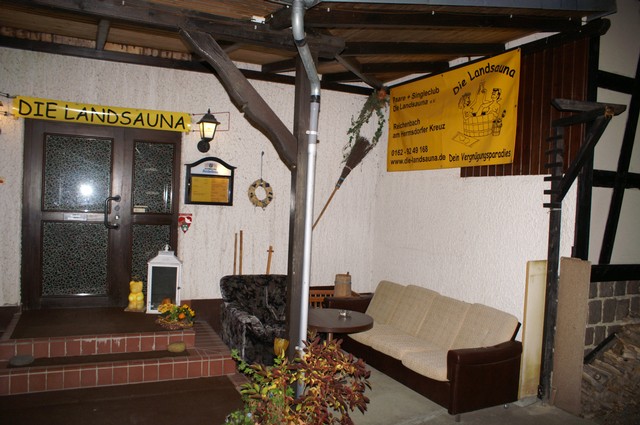 Eingang mit Glastür, gelbem Banner und einer Sitzecke davor.